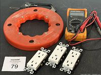 Full lot display including the orange cable reel, Klein Tools multimeter, and three white electrical outlet receptacles on a black surface.