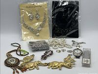 Mixed assortment of jewelry including necklaces, bracelets, earrings, a watch, and rings on a white background.