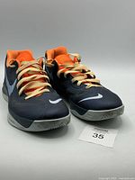 Front view of Nike Zoom Hyperfuse basketball shoes showing black upper with orange lining and beige laces.