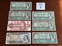 Full overview of all eight banknotes showing multiple one dollar bills and one two dollar bill, laid out on a wooden surface