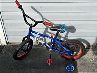 Side profile of the Paw Patrol children's bicycle showing blue frame, Paw Patrol decals, black and red wheels, red pedals, and attached training wheels.