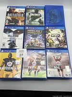 Front view of 8 PS4 game cases showing cover art including Battlefield Hardline, Call of Duty, Killzone, Minecraft, Plants vs Zombies, Madden, FIFA, and NHL. One blue case is empty.