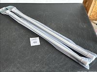 Two white window tension rods in packaging laid on black surface