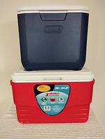 Two stacked Coleman coolers: red 36 quart cooler on bottom and navy blue smaller cooler on top.