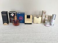 Photo shows assorted fragrances in boxes and bottles alongside sealed cosmetics on a surface with cloth texture.