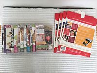 Twelve Anita Goodesign embroidery CDs arranged in a row with colorful labels showing various embroidery projects, next to four sealed packs of printable quilting fabric sheets with red packaging from The Electric Quilt Company.