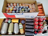 Box containing multiple cones of embroidery thread in assorted colors, some wrapped in plastic.