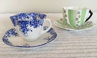 Shelley and Thomas Forester & Sons bone china teacups with saucers on white textured fabric background, showing two distinctly patterned cups and matching saucers.