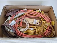 Box containing assorted extension cords in various colors and two power bars, one with a red switch.
