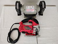 Photo showing both Skil jigsaw and Brico bench grinder from above on a white textured surface