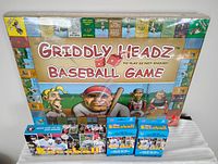 Photo of unopened Griddly Headz Baseball board game and three boxes of MLB baseball cards on a white surface.