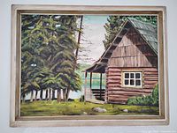 Frontal photo of the painting depicting a rustic cabin, surrounding trees, lake, grass and rocks in a wooden frame.