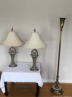 Two tri-lite table lamps with original shades and a vintage Torchiere lamp standing side by side. The tri-lite lamps feature decorative metal bases with a pineapple motif and finials on the shades.
