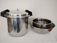 Mirro 22 quart pressure cooker/canner with lid and 3 nested stainless steel mixing bowls side by side on white surface