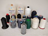 Full lot of specialty thread cones including nylon monofilament and various colored threads on cones, arranged on white fabric