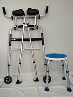 Front view of the aluminum upright folding walker and blue seat shower stool placed on a white cloth against a light wall.