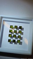 Photo of 12 calibrated princess cut green tourmaline gemstones arranged on a white tray under light showing the stones' bright green color and clarity.