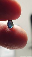 Close-up of the natural sapphire showing teardrop briolette cut and blue-green hues held between fingers.