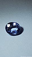 Close-up image of the oval cut cornflower blue sapphire on a plain surface showing color and facets.