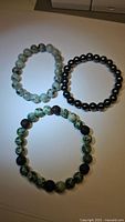 Top down photo of three stretchy natural gemstone bead bracelets, showing the dark hematite beads, green spotted jasper, and green lavastone beads.