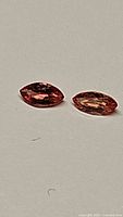 Close-up photo of two marquis cut natural Padparadcha sapphires lying flat on a neutral background, showing color and facets.