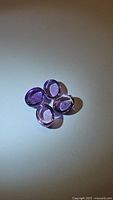 Four oval cabochon cut amethyst stones arranged closely on a flat surface under bright light to show clarity and color.