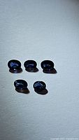 Five oval cut natural blue sapphires laid out on a flat surface with light reflections highlighting facets and color.