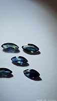 Photo showing five marquis cut natural blue sapphires of various blue shades under direct light, highlighting their clarity and faceting.