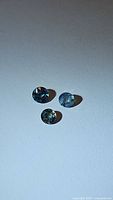 Three natural blue sapphires positioned on a white surface showing round cut and internal characteristics.