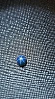 Natural round cabochon blue star sapphire on textured black surface showing 6-ray star flash