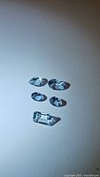 Five natural aquamarine gemstones in various cuts positioned on a light background showing different sizes and clarity.