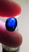 Close-up photo of a faceted deep royal blue oval iolite gemstone held between fingers, showing color and clarity under light.