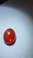 Close-up image of oval cabochon-cut deep fire orange natural Ethiopian fire opal on a plain light background showing internal reflections and color play.