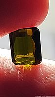 Close-up photo of the octagon-cut green tourmaline gemstone held between fingers, showing its deep green color and clarity.