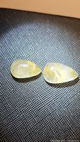 Two polished pear-shaped gemstones resting on a textured surface, showing internal golden rutile needle inclusions.