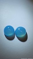 Pair of two natural round cabochon icey blue chalcedony gemstones, approximately 10mm diameter each, showing smooth polished dome surface and translucent icy blue coloration.