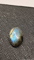 Oval cabochon natural labradorite gemstone with golden and blue flashes on textured surface background.