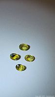 Photo of four oval shaped yellow to slightly blue sapphires on white background, faceted and calibrated in size.