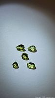 Five natural Peridot gemstones of different cuts and sizes laid out on a white background showing varied faceting and clarity.