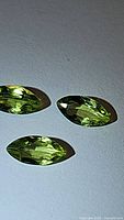Close-up of three marquis cut natural peridot gemstones on a flat surface.