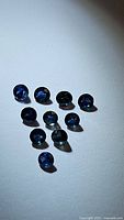 Multiple loose round-cut natural royal blue sapphires arranged on a flat surface with visible facets and reflections.
