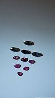 Photo of six blue-green marquise-cut sapphires and six small faceted rubies in pink/red hues on a white background.