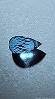 Clear close-up of pear-shaped fancy briolette cut Swiss blue topaz gemstone showing intricate facet pattern and rich blue hue.