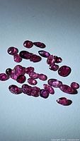 Photo showing multiple small untreated ruby gemstones scattered on surface, highlighting color and inclusions.