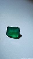 Rectangular emerald cut vivid green onyx gemstone, showing translucency and rich green color on a light background.