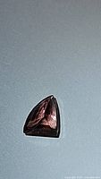 Triangular cut padparadscha sapphire gemstone on a grey background