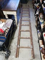 Long wooden extension ladder laid flat on floor in storage area, showing two sections and many wooden rungs.