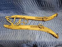 Photo of an antique wooden ox harness with carved wooden pieces, metal rings, and leather straps spread on a quilted blanket surface.