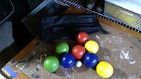 Photo shows eight bocce balls of four different colors and one small white target ball arranged on a tabletop with a black carrying bag visible behind.