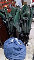 Three green camping cots folded together with blue sleeping bag in carrying sack in front.